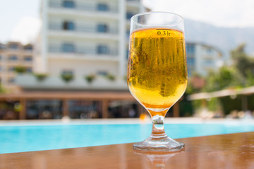 glass of beer on the table on the background of the pool and the hotel