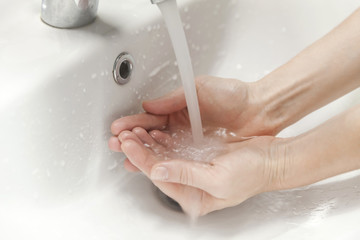 Hands cupping running water under bathroom sink faucet, hygiene concept