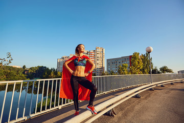 Girl runner in a superhero costume on the road in the city in the summer.