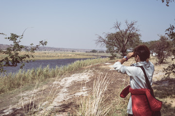 Tourist watching wildlife by binocular on Chobe River, Namibia Botswana border, Africa. Chobe National Park, famous wildlilfe reserve and upscale travel destination. Toned image.