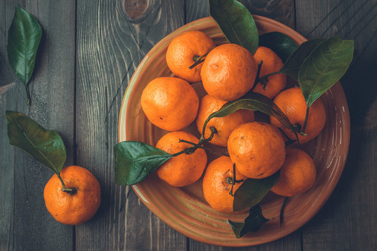 Ripe mandarine with leaves, tangerine mandarine orange on wooden table background. Citrus fruits Mandarins in plate. Top view, copy space