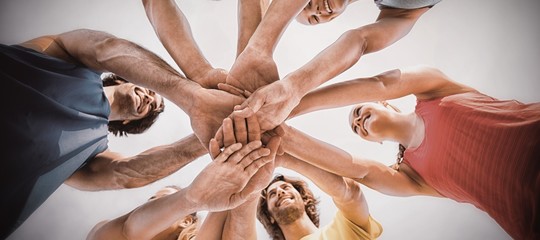 Friends standing with stacked hands against sky
