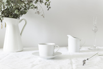 mesa con jarron de flores, taza de cafe y lechera en blanco