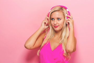 Happy young woman with headphones on a pink background