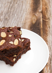 Sliced brownies with almond sliced topping on white plate over wooden table. Favorite dessert for chocolate lover.