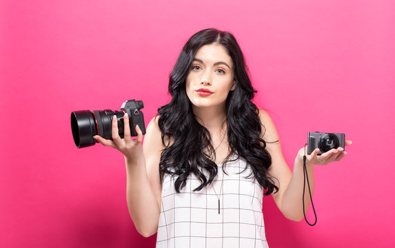 Young woman comparing professional and compact cameras on a solid background