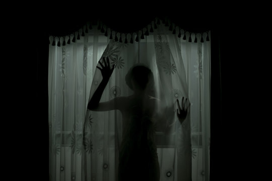 Scary human body silhouette woman front of window behind the black curtain.