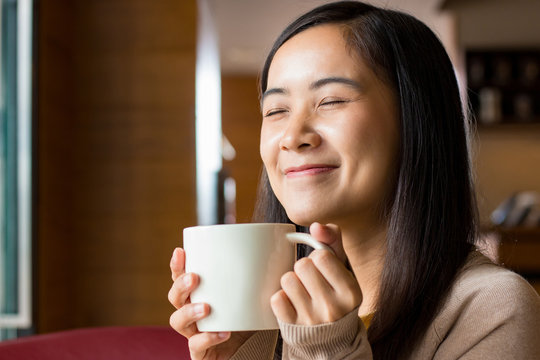 Asian woman drinking coffee from white coffee cup with blurry background of coffee shop