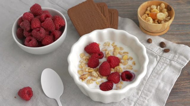 Healthy breakfast - yogurt or milk with raspberry berries, cereals or gorp, chocolate cakes. Top view. Camera locked down. 