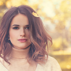 Beautiful Autumn Model Woman with Curly Bob Hairdo and Fall Maple Leaf Outdoors