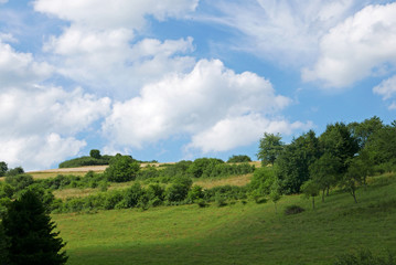 Fototapeta na wymiar Menschenleere sommerliche hessische Mittelgebirgslandschaft im Sonnenschein mit Schäfchenwolken