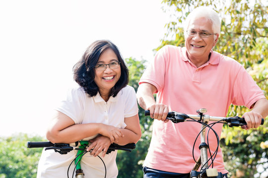 Portrait of active senior couple smiling while standing on bicycles outdoors in summer