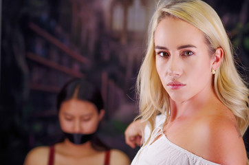 Fototapeta premium Young mad american blonde woman, exhorting to a latin woman to leave the country, using her arm and pointing to her, racism, violence or discrimination concept