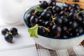 Fresh blackberries (black currant) in ceramic bowl on white wooden table, selective focus