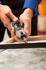 Closeup of a hardworker man using a polisher in a wooden frame, on a gray table in a blurred background