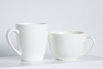 Two white mugs, clean tea and coffee cups of  different size and design