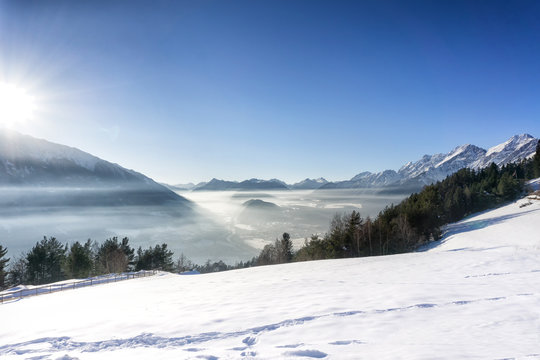 Winter mountain lanscape. Blue sky with bright sun, fog in the valley. Tirol, Alps, Austria.