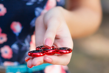 A girl is holding a popular toy fidget spinner in her hands. Stress relief. Anti stress and relaxation fidgets, spinner for tired people. Girl playing with a red fidget spinner.