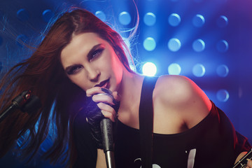 Beautiful girl with a microphone and a guitar in hand on stage singing a song in rock style, closeup