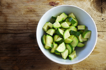 sliced zucchini in a white bowl on a rustic wooden background with copy space, preparing vegetables...