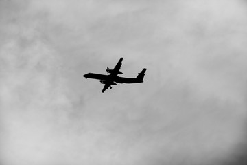 Plane silhouette on a cloudy sky, in black and white.
