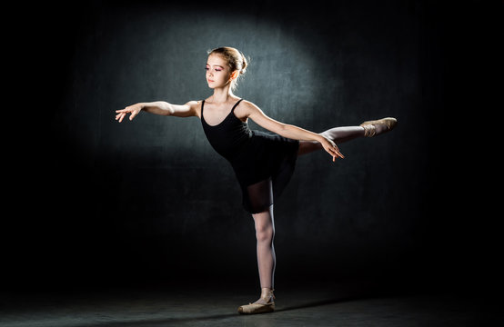 Beautiful young ballerina posing and dancing in the studio on a dark background. A little dancer.