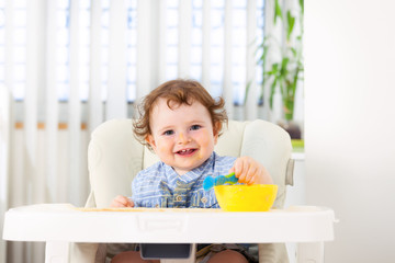 Cute baby boy eating by himself on high chair