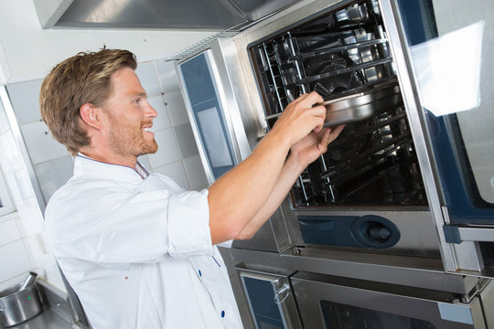 smiling handsome male cook holding dish in the restaurant kitchen