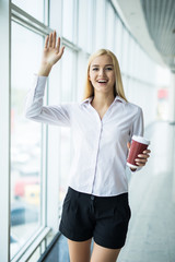 Fototapeta premium Businesswoman welcomes with cup of coffee in other hand near big panoramic window in the office