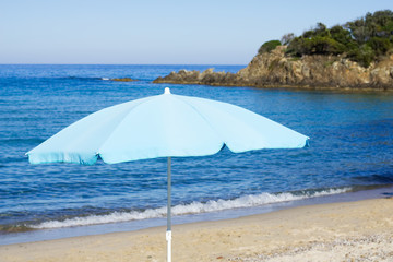 Fototapeta na wymiar Blue parasol on sunny beach at Corsica, France. Beach umbrella. 