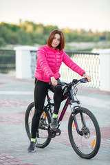 Fototapeta premium Adult beautiful redhead woman with bob haircut posing on bicycle in autumn city river pier