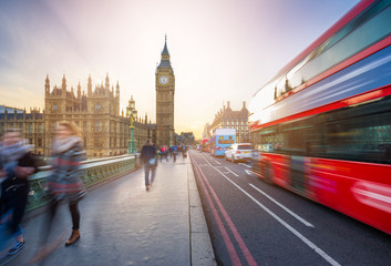 Obraz premium London, England - The iconic Big Ben and the Houses of Parliament with famous red double-decker bus and tourists on the move on Westminster bridge at sunset