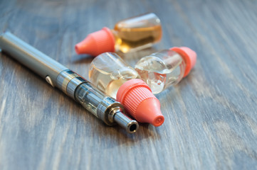 An electronic cigarette, a vape, and several bottles of liquid for refilling lie on a wooden background.