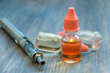 An electronic cigarette, a vape, and several bottles of liquid for refilling lie on a wooden background.