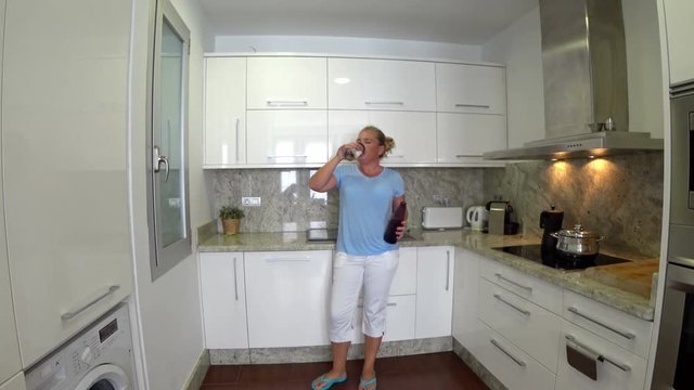 Blonde smiling woman standing in her kitchen drinking fresh  water