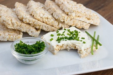 Bitten off rce cake with cream cheese and chives on white plate. Concept of healthy, low fat, weight reducing diet