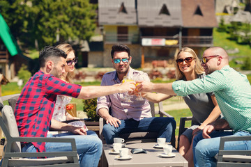 Beautiful stylish friends are using a digital tablet, drinking coffee and smiling while resting in the park
