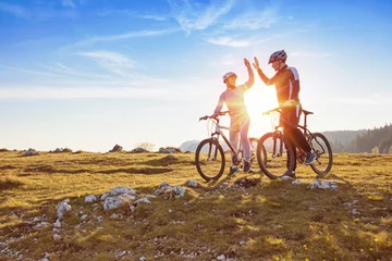 Foto op Canvas happy couple goes on a mountain asphalt road in the woods on bikes with helmets giving each other a high five © FS-Stock