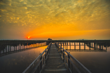 Beautiful romantic golden sunset and wooden bridge at pond. Fantastic vivid twilight at Sam Roi Yod National Park, Prachuap Khirikhan, Thailand.
