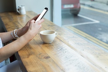 Cropped image of young woman using phone while sitting in cafe