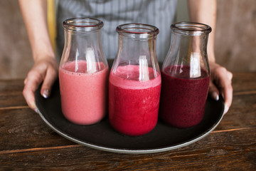 Waiter brings bottles of smoothie on black tray. Fruit drinks from strawberry, cherry and wineberry, refreshment in summer period, healthy food close up picture