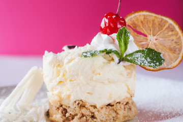 Creamy orange dessert serving on crimson background in restaurant. Delicious cake decorated by dried citrus, cherry and mint, real pleasure of sweets. Close up picture