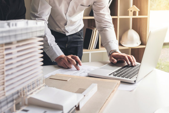 Engineering Or Creative Architect In Construction Project, Engineers Hands Working On Construction Blueprint And Building Model At A Workplace In Office, Building And Architecture Concept