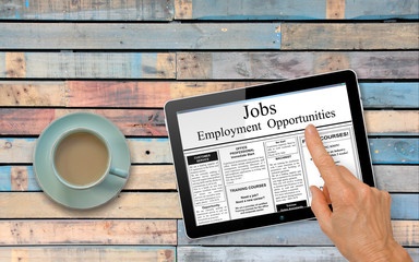 Online job hunting Hand with computer tablet reading employment ads on table with coffee