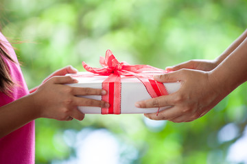Hands of parent giving Christmas gift to child girl on green nature background. Christmas concept.