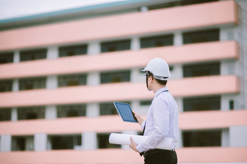smiling young architect or engineering builder in hard hat with tablet over group of builders at...