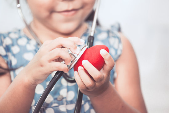Cute asian little child girl with stethoscope playing doctor to listen red heart in hand