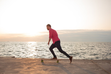 skater in red shirt and blue jeans riding on concrete pier on longboard during sunrise, sea or ocean background  