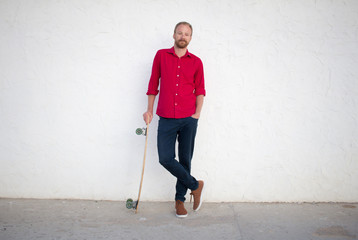 Young bearded man riding on skateboard, hipster with longboard in red 
shirt and blue jeans urban background  