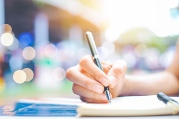 Woman's hand writing on a notepad with a pen on a wooden desk.